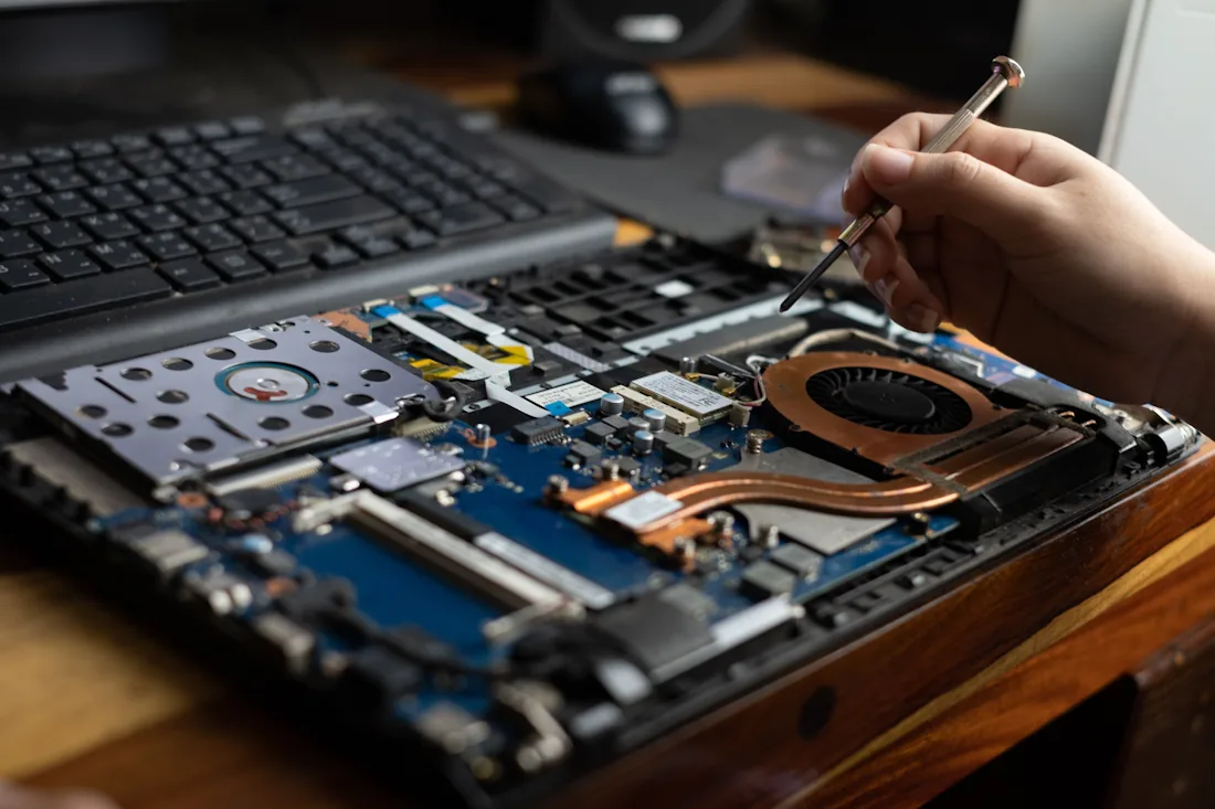 Fachmännische Laptop-Reparatur bei softwelop: Nahaufnahme einer Technikerhand mit Schraubenzieher am Mainboard.